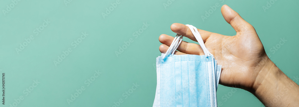 Fototapeta premium Close-up of male hand holding medical flu masks preventing coronavirus on background of cyan, aqua menthe color with shadows.