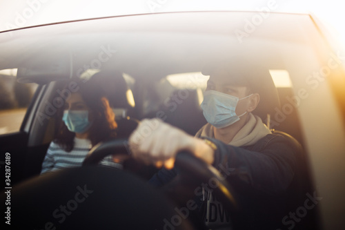 Boy and girl driving a car wearing sterile medical mask. Taxi driver with a passanger stuck in a traffic jam during coronavirus quarantine isolation in the city. Prevernt spread of covid-19 concept.