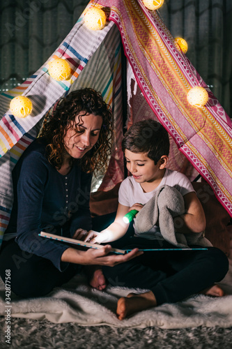 Mother and son reading a book on a tent at home