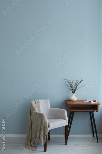 Cozy interior of retro armchair vintage wooden table with magazine and vase on it on the background of the blue wall and wooden floor. Copy space on the top