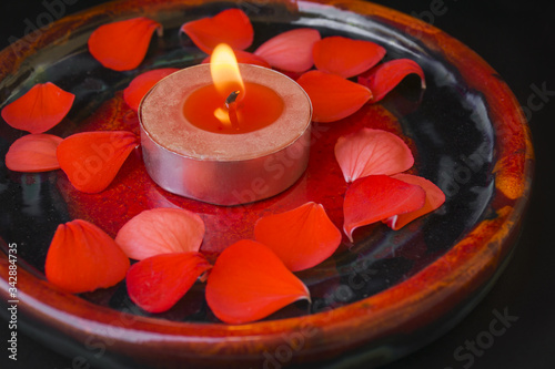 Beautiful romantic decoration with red aroma candle and rose petals on red and black plate. Colours of passion, desire and love.