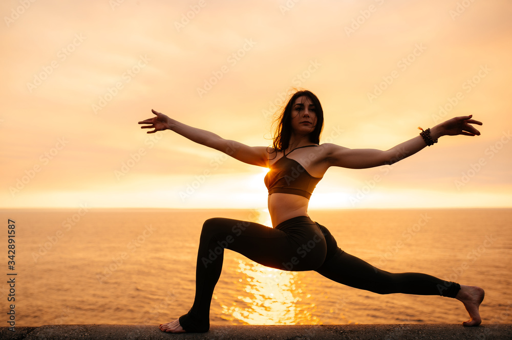 A girl practices yoga by the sea during a beautiful sunset. Fitness and healthy lifestyle