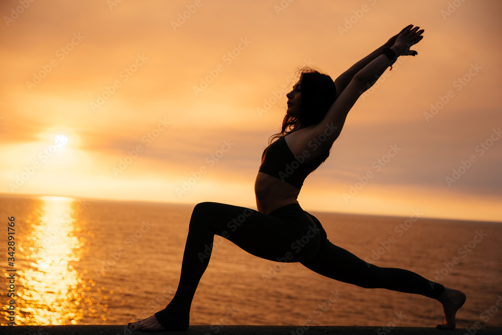 Silhouette of a young girl who practices yoga by the sea at sunset. Yoga Lifestyle