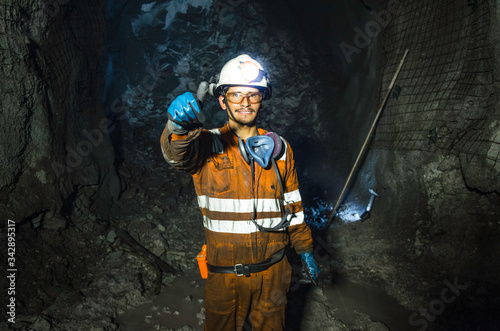 Miner in the mine. Well-uniformed miner inside mine raising thumb, conceptual photo photo