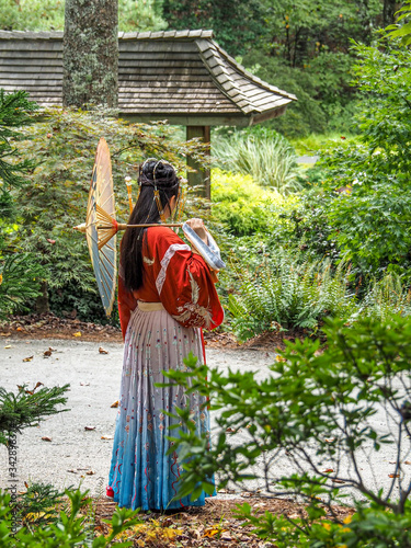 Young woman posing with umbrella in traditional Chinese clothing in Japanese garden.