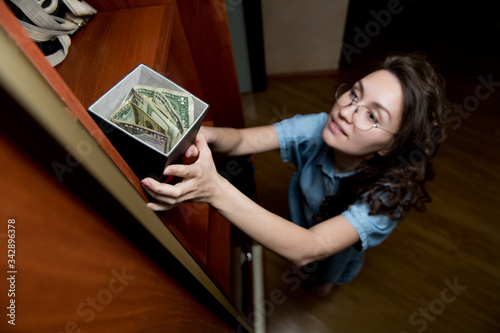 A young woman takes or takes a stash of money from the top shelf of a closet