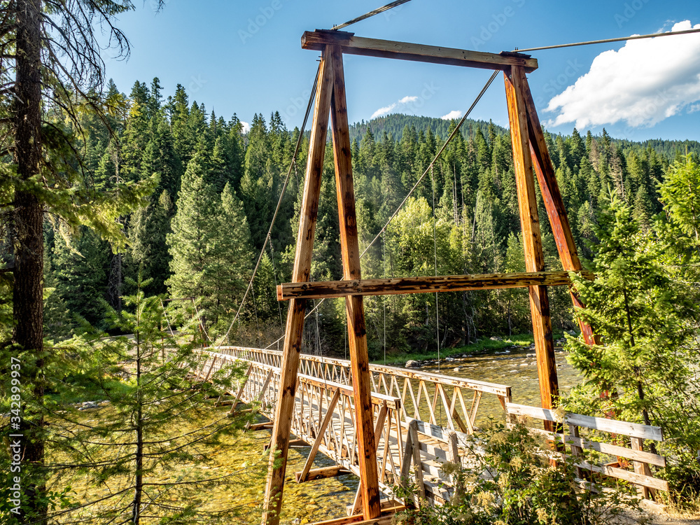 Fototapeta premium Wooden pedestrian bridge suspended over mountain stream