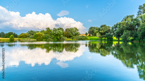 Rural summer landscape reflected in the pond. Blue sky, white clouds and lush green trees