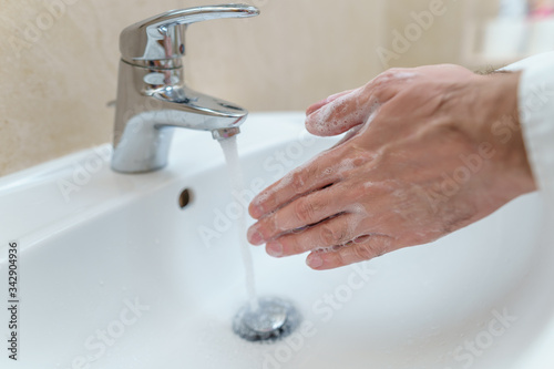 Young man washing hands at home cleaning hand under running water in bathroom sink. House, lifestyle.