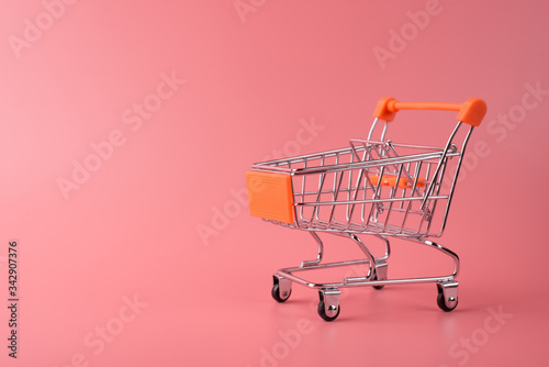 Photo of small silver shopping cart isolated over pink color pastel background with copy empty blank space