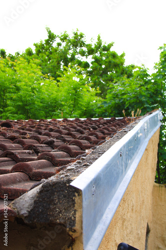 Close-up on hollow tiles of red terracotta, covered with moss and vegetation. Old roof mechanical roof cover. Zinc protection on the corner of the roof. Solin