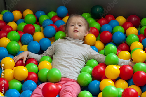 Happy little girl having fun in ball pit in kids indoor play center
