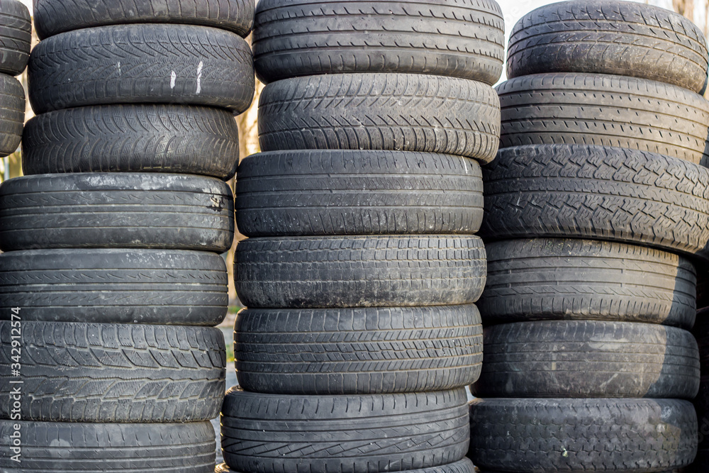 A stack of old rubber wheels lies on the street in several rows. Used black tires. A stack of old rubber wheels lies on the street in several rows. Used black tires.