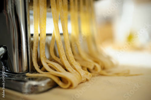 Staying at home with your family and preparing fresh home-made pasta  tagliatelle   pasta machine on a wooden board cutting sheets of pasta into noodles.