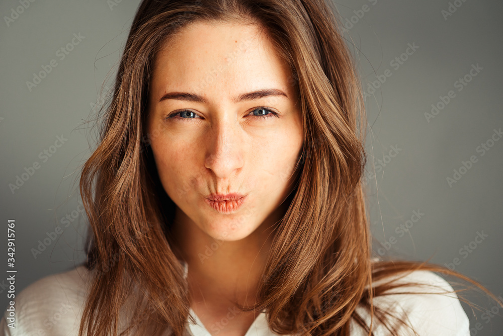 Naklejka premium Serious girl with a gaze and closed lips in a tube on a gray background, close-up. Nude makeup, without retouching.