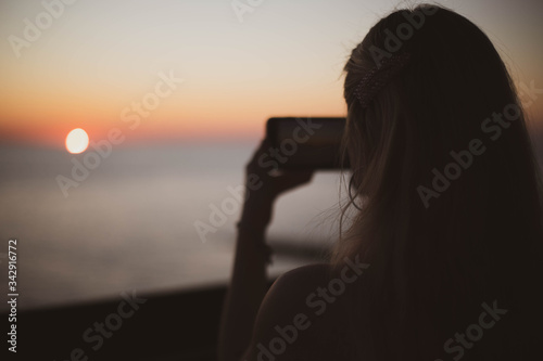 Beautiful blonde girl shoots sunset on her phone.