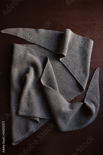 brown knitted triangular scarf lies on the table, table brown texture