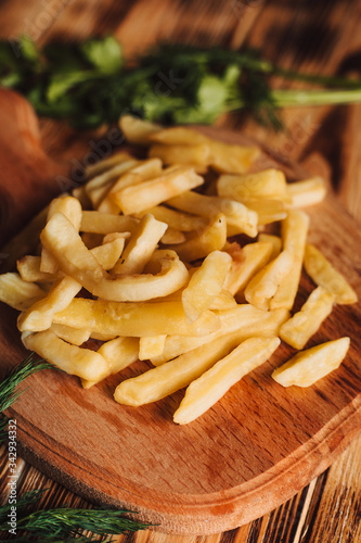 Tasty french fries on cutting board, on wooden table background with dill