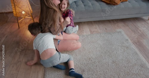 Young happy beautiful Caucasian single parent mom having fun bonding with two cute kids, hugging and tickling at home.
