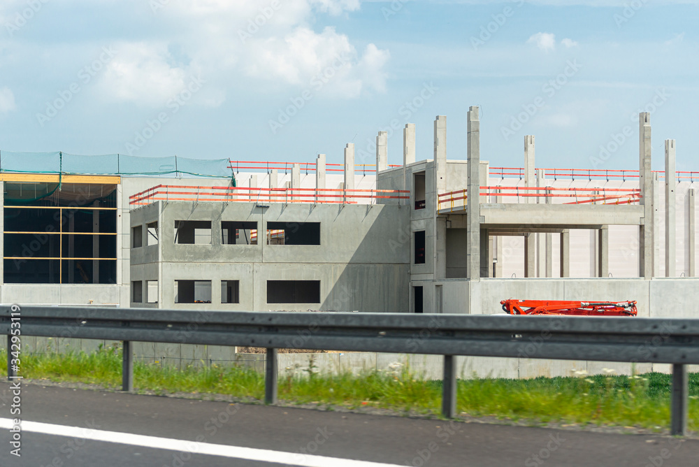 Construction of a modern hall made of concrete slabs, visible concrete poles, construction site on the expressway.