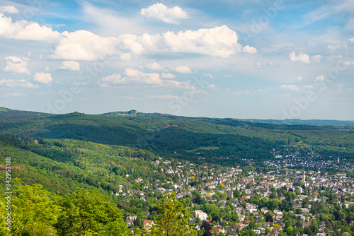 Landscape of green forest on the hills in summer with blue sky and white clouds. Visible city buildings, photo taken in West Germany.