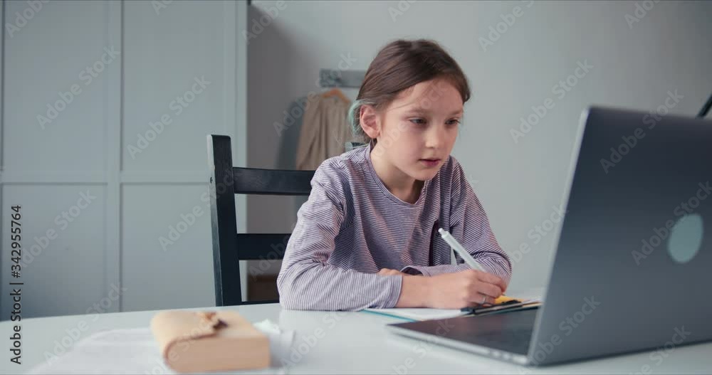 Self isolation and school online, cute Caucasian teen age girl writes down task from remote tutor via laptop webcam app. Self isolation and school online, cute Caucasian teen age girl writes down task from remote tutor via laptop webcam app.
