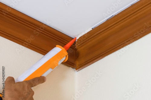 Technician man hand using glue gun or manual caulking gun with polyurethane silicone to repair and fix the wooden cornice with the ceiling. Installation or renovation interior concept. 