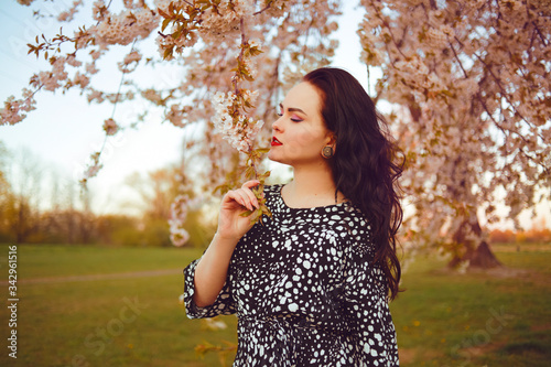 Fashionable stylishly dressed girl on a background of a tree with inflorescences  walks in the park on the street. Brunette model poses and enjoys nature. Spring