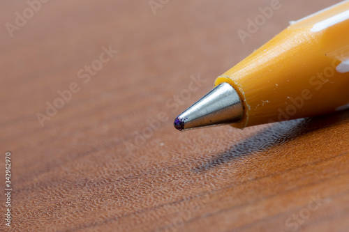 Ballpoint pen nib close-up. It is yellow and brown on the table.