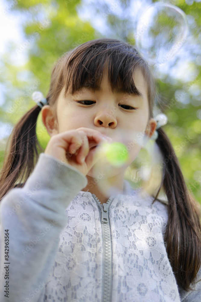 緑の中でシャボン玉で遊ぶ幼児(5歳児)
