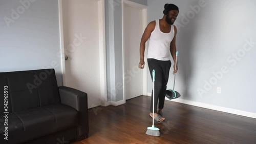 Cool black  man cleaning the house with broom. African american man on quarantine use broom to swep his flat. Funny concept photo