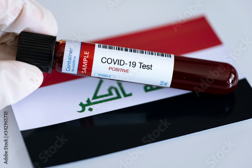 Testing for presence of coronavirus in Iraq. Tube containing a blood sample that has tested positive for COVID-19. Iraqi flag in the background.