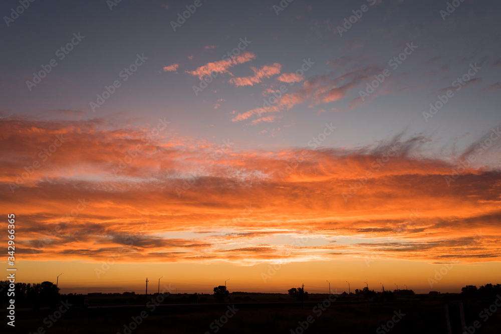 Sunset landscape, an orange bright sky and small silhouettes on the horizon