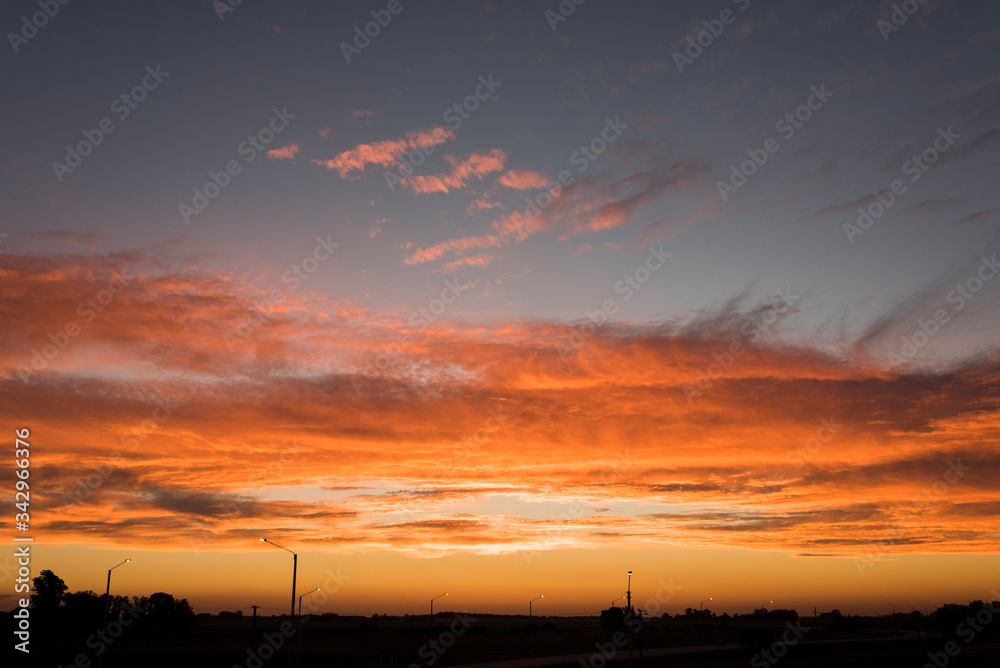 Sunset landscape, an intense orange sky and small silhouettes, as lighting poles Sunset landscape, an intense orange sky and small silhouettes, as lighting poles