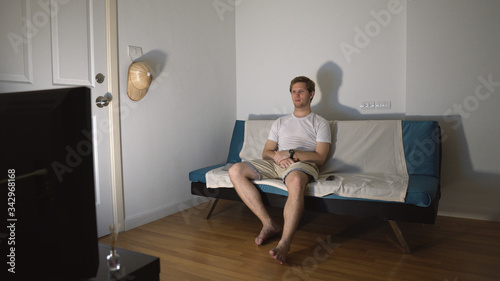 Young Man Sitting on Couch and Watching TV Alone at Night Being Entertained