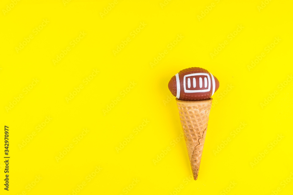 Rugby ball toy in ice cream waffle cone on yellow background in minimal style. Concept sports entertainment. Top view Copy space Template for text or your design. Rugby ball toy in ice cream waffle cone on yellow background in minimal style. Concept sports entertainment. Top view Copy space Template for text or your design.