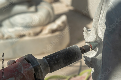 Burmese stone engraver uses a marble grinding machine to carve white marble  photo