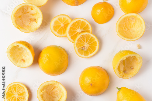 High angle shot of lemon rinds, whole lemons and lemon slices on a white marble kitchen surface.