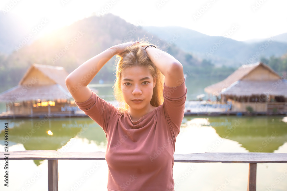 Portrait of asian girl are sitting on the wooden floor and looking the sunset over the mountain at rural Thailand. Beautiful asian women are looking view of nature.
