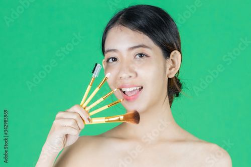 Beauty young Asian woman holding makeup brushes over green isolated background. Healthy and cosmetics concept.