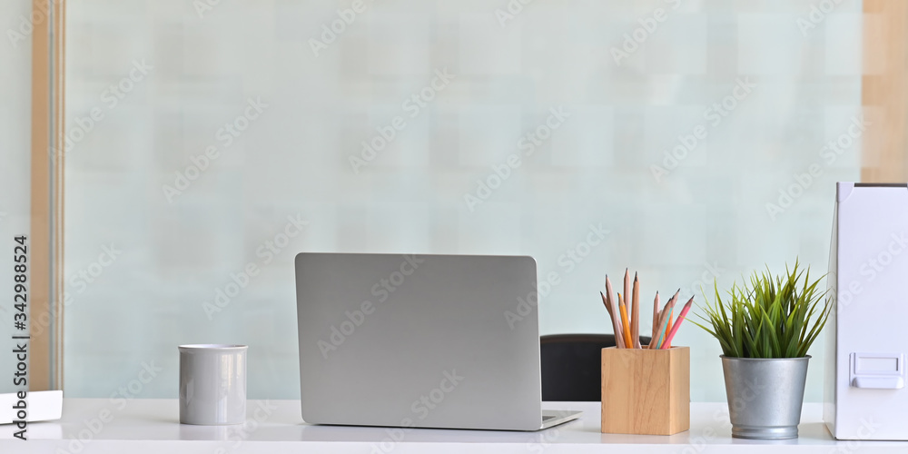 Photo of Computer laptop that putting on white working desk and surrounded by coffee cup, document file, wooden pencil holder and potted plant. Orderly workspace concept. Photo of Computer laptop that putting on white working desk and surrounded by coffee cup, document file, wooden pencil holder and potted plant. Orderly workspace concept.