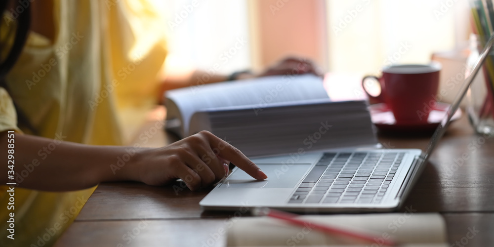 Closeup woman relaxing and using a computer laptop while sitting at the wooden working desk over comfortable living room windows as background. Student tutoring and online learning concept. Closeup woman relaxing and using a computer laptop while sitting at the wooden working desk over comfortable living room windows as background. Student tutoring and online learning concept.