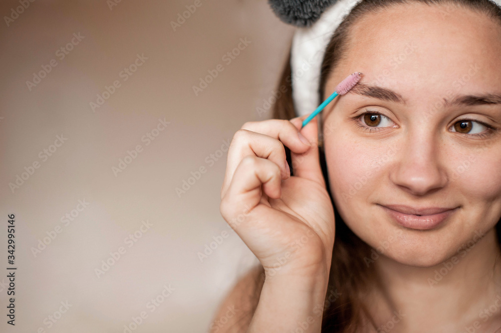 a brunette girl without makeup with problematic skin with a bandage with ears on her head naked wrapped in a towel after a bath doing Spa treatments brushes her eyebrows