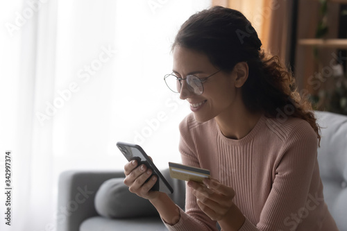 Side view happy female client holding plastic credit card in hands, ordering food, taxi or plane tickets in mobile application, satisfied with user friendly interface, easy technology e-banking usage.