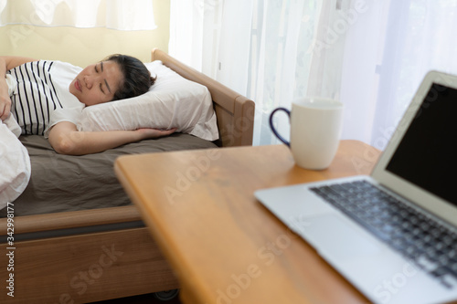 A young asian woman is sleeping late in the bed after stay home and working remotely at night as a social distancing protocol during covid-19 or coronavirus pandemic. business and technology concept
