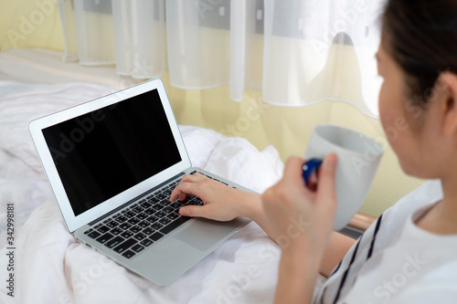 A young asian woman is working remotely on the bed in the bedroom as a social distancing protocol during covid-19 or coronavirus pandemic. business and technology concept