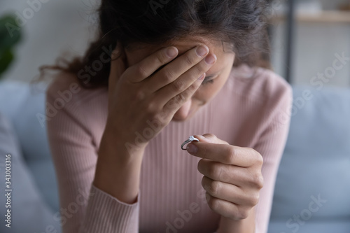 Close up focus on frustrated desperate millennial woman holding engagement ring in hand, denied getting married. Stressed young girl making decision breaking up with fiancee, betrayal divorce concept.