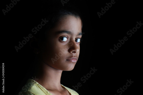 Portrait of an Indian little girl with short hair. Beautiful eye of a child on black background. Dramatic look of a little girl in India.