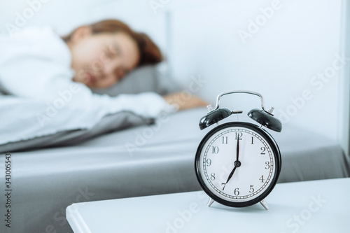 Close up Clock on the bed Asian woman wake up and disturbed by alarm clock early morning