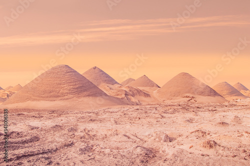 A beautiful warm and pinkish background travel image of many sandy dunes  pyramids or hills under a cloudy sunset and some sandstorm dust in asia or africa with copy space